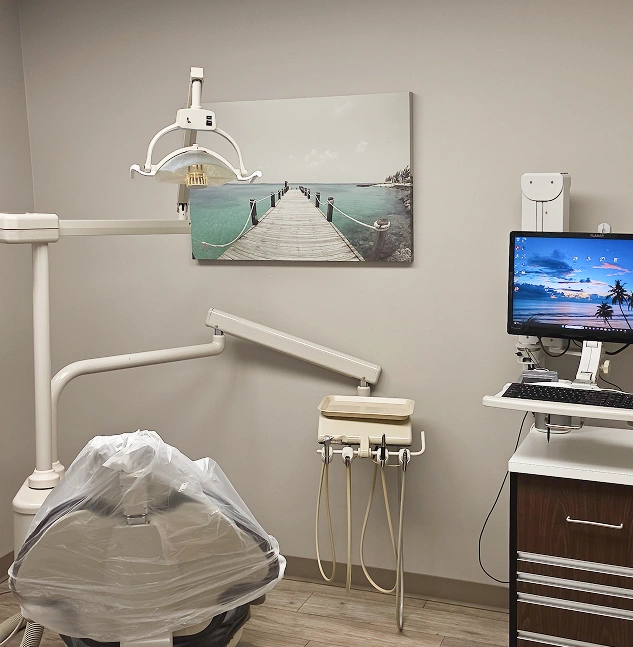 Dental treatment room with a dental chair, overhead examination light, dental equipment, and computer monitor.